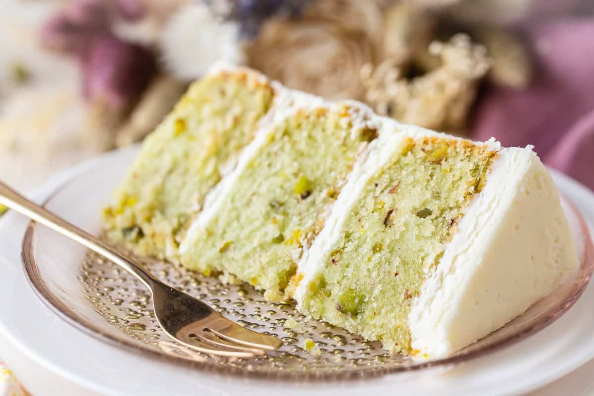 A slice of pistachio cake on a plate with a fork.