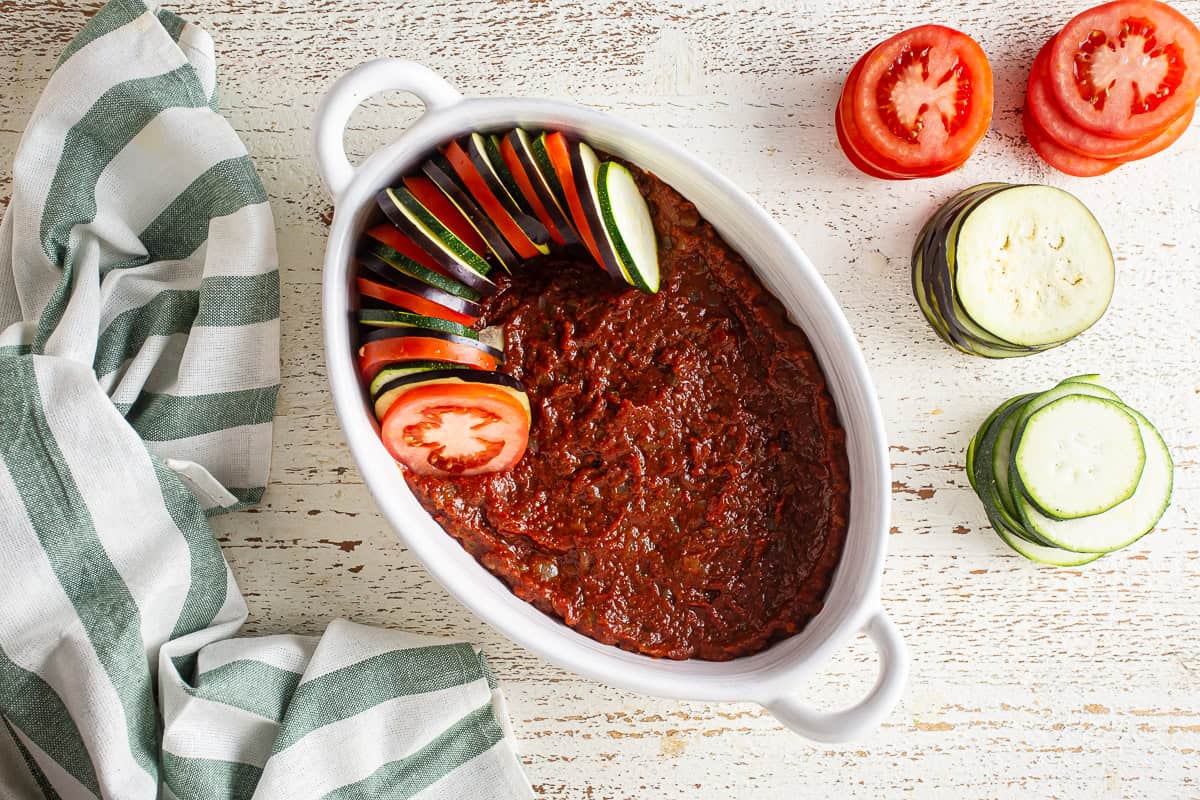 Layering sliced vegetables over the sauce in a casserole dish for ratatouille.