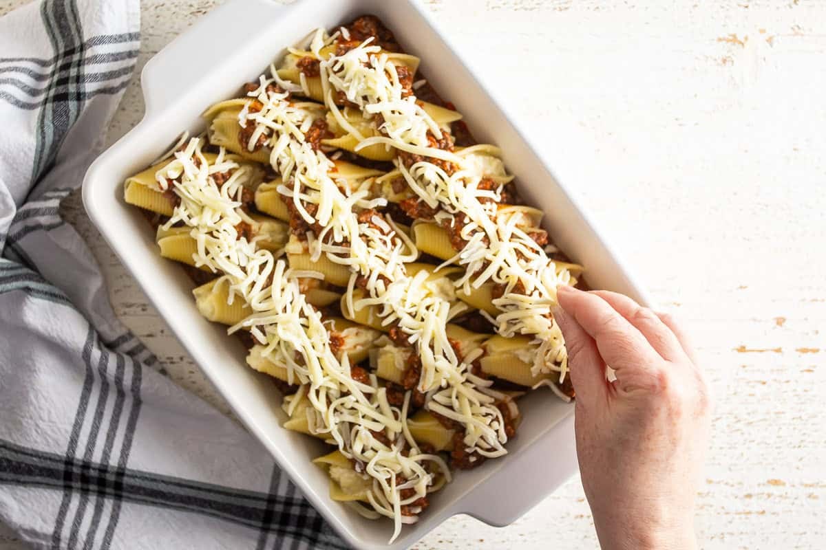 Adding shredded cheese to stuffed shells before baking