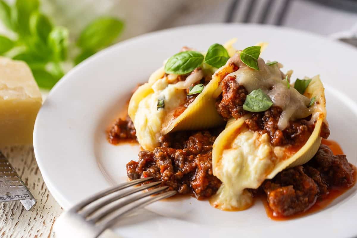 Stuffed shells on a white plate with fresh basil leaves on top