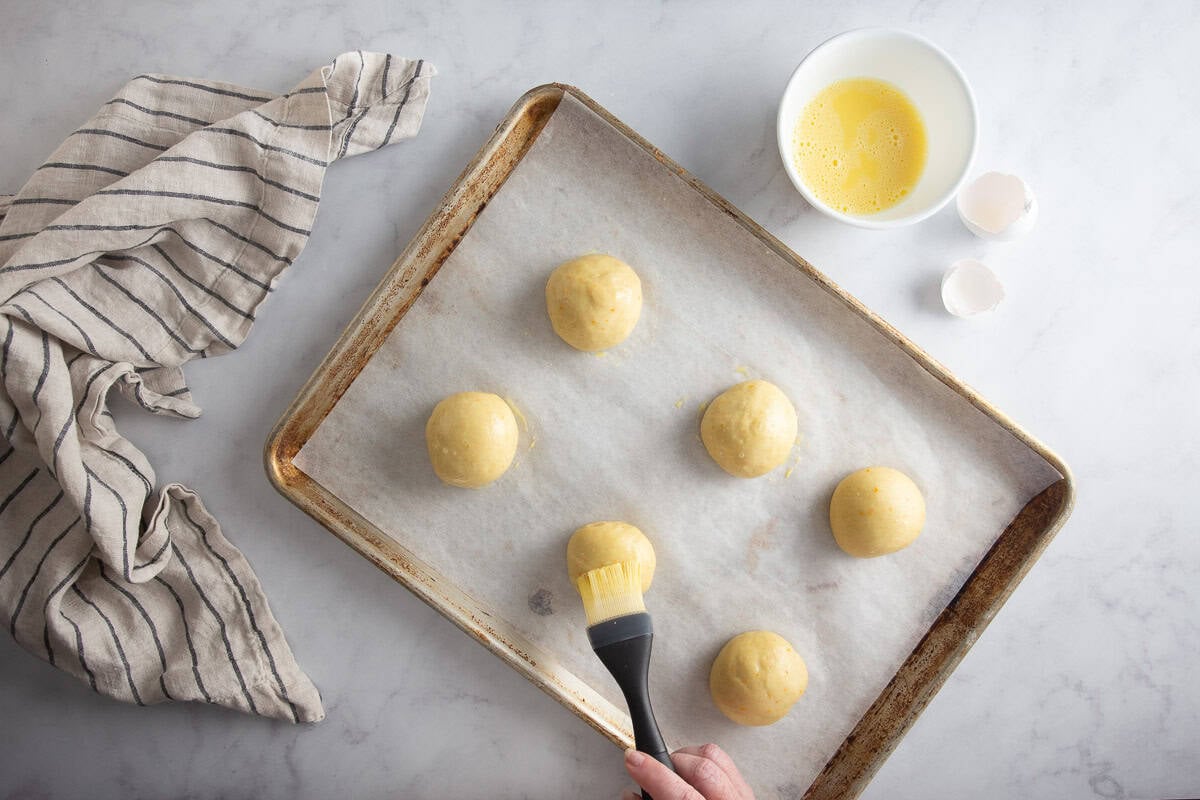 Glazing the risen maritozzi on a prepared baking sheet.