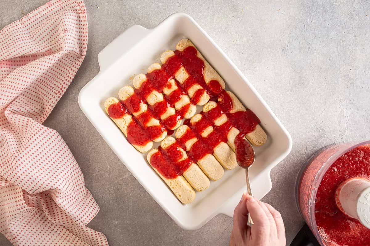 Pouring strawberry filling over ladyfingers for strawberry tiramisu.