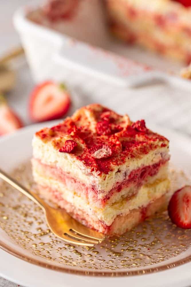A slice of strawberry tiramisu on a plate with a gold fork.
