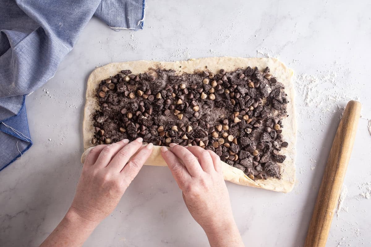 Rolled out pastry dough with cookie croissant swirl filling spread on top, being rolled up