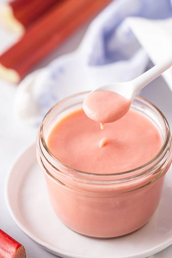 Rhubarb curd in a glass jar with a white spoon.