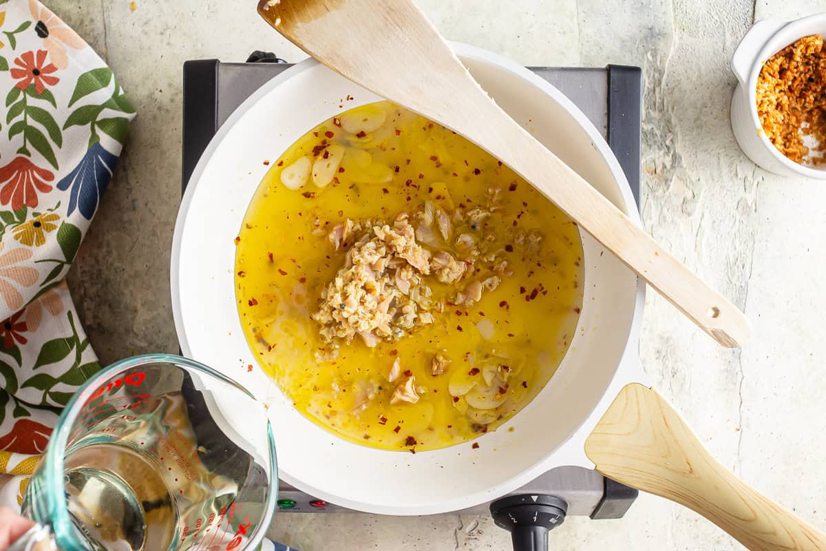 Adding white wine to the oil and garlic and chili flakes for clam sauce.
