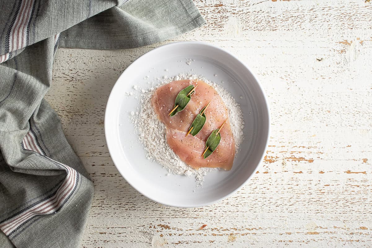 Dusting a chicken breast for chicken saltimbocca with flour.