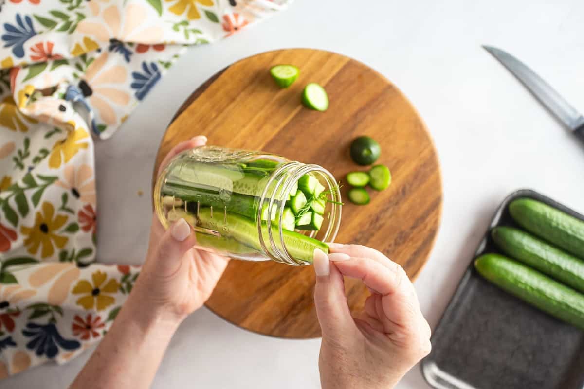Stuffing sliced dill pickles on a glass canning jar.