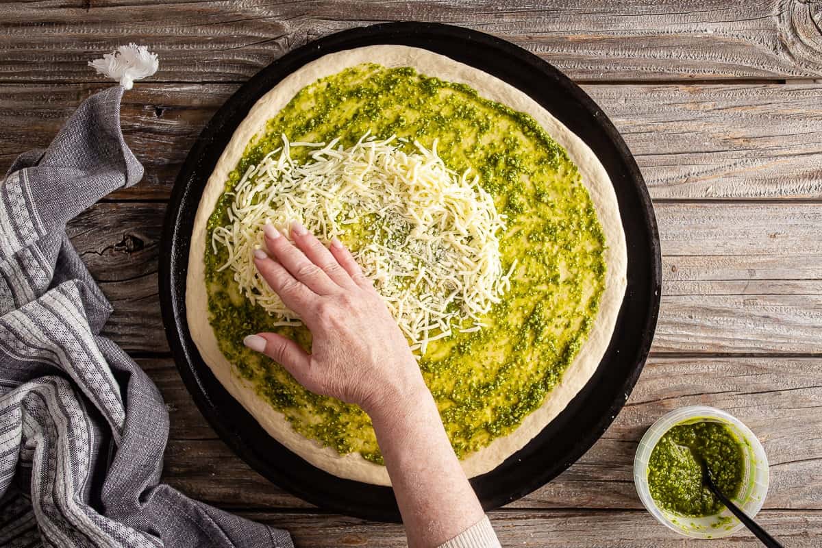 Sprinkling mozzarella over a pesto topped pizza crust