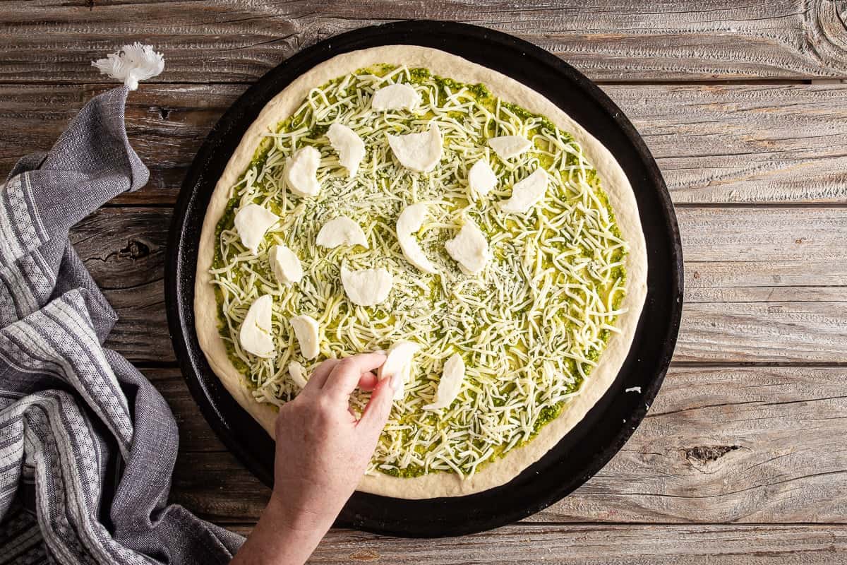 Adding fresh mozzarella to a pesto pizza