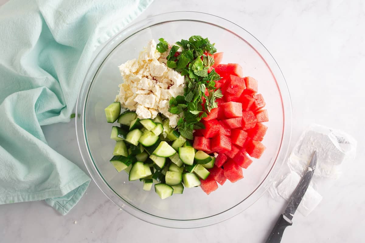 Ingredients for watermelon salad in a glass bowl before being mixed.
