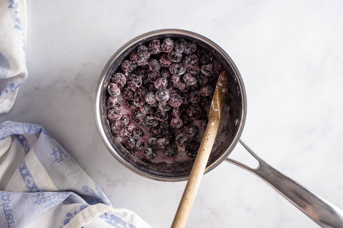 Blueberries coated in sugar and cornstarch in a pot with a wooden spoon.