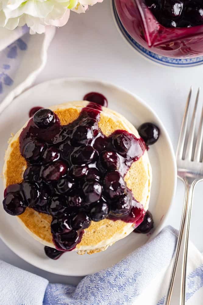 Blueberry syrup on pancakes on a white plate.