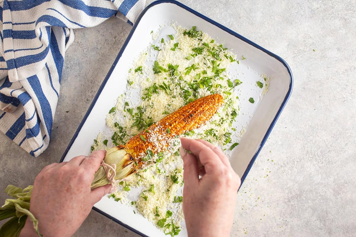 Adding cheese and cilantro to the elote before serving.