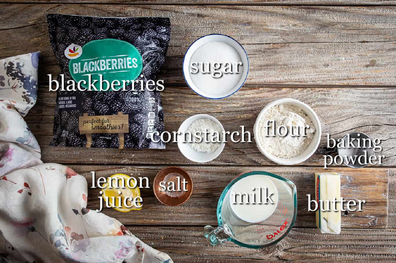 Ingredients for blackberry cobbler on a wooden background in separate containers.