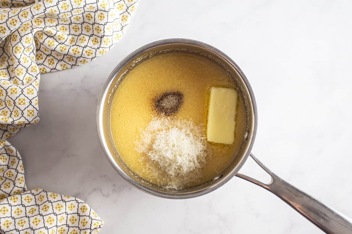 Adding butter, cheese, and seasonings to the polenta mix in a pot