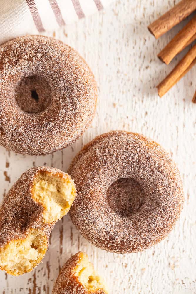 Close-up of cinnamon sugar donuts with one broken open on a white wooden surface.