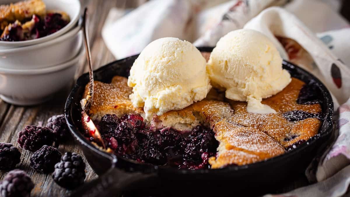 Baked blackberry cobbler in a cast iron skillet with ice cream on top.