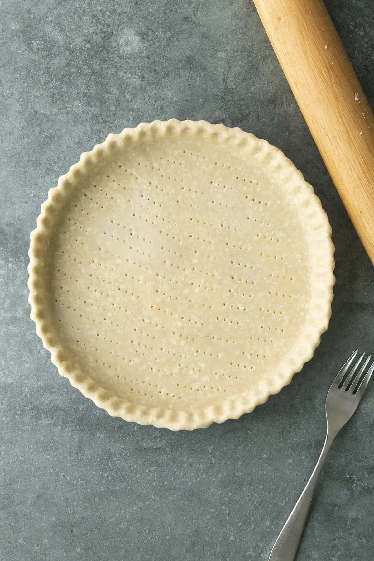 Unbaked pie crust in a tart pan with rolling pin and fork