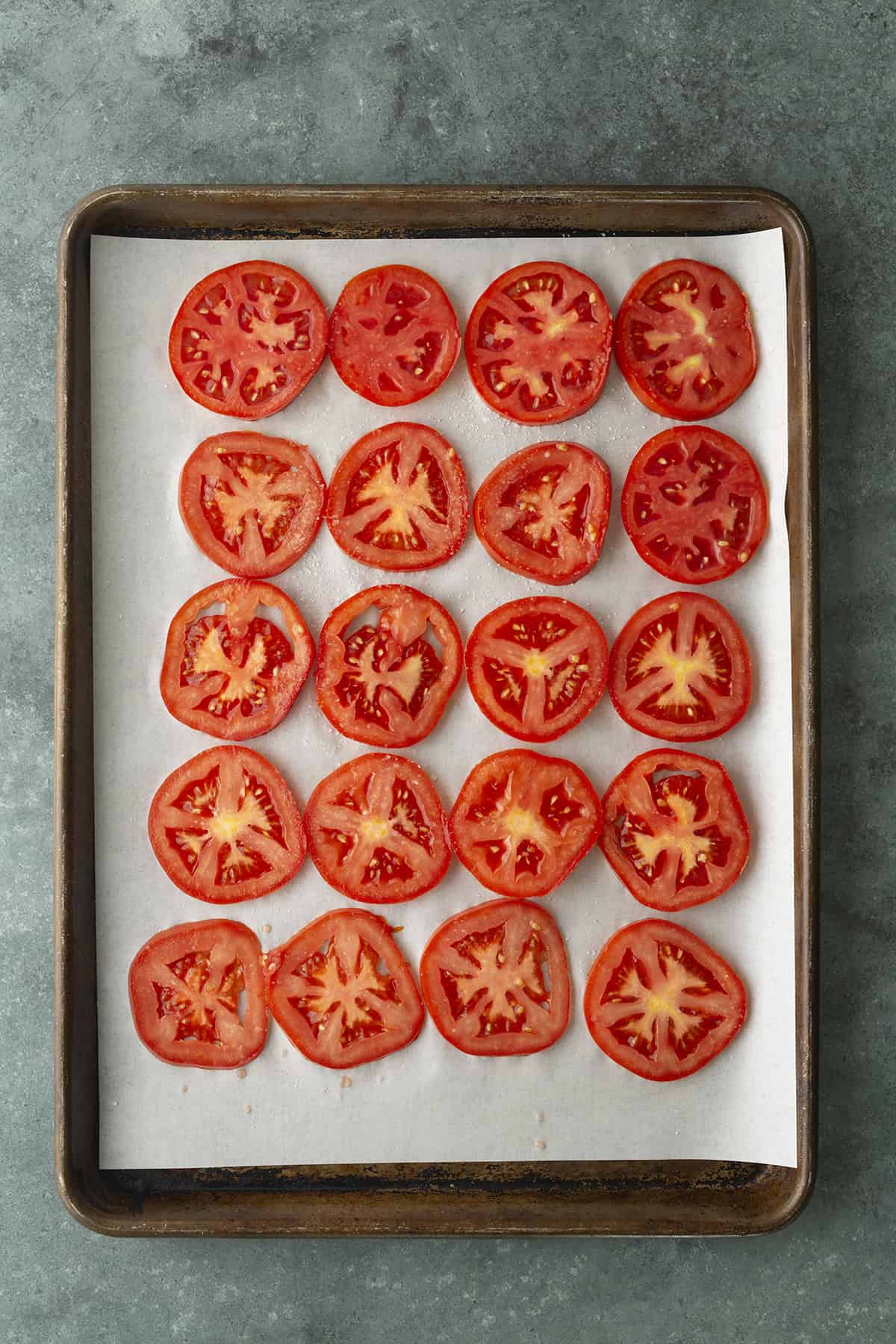 Sliced tomatoes on a sheet pan lined with parchment