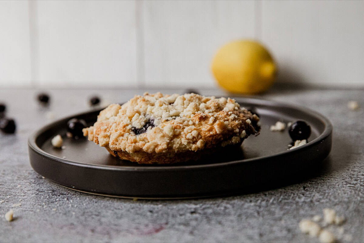 Close-up of a blueberry streusel muffin top on a black plate with a lemon in the background.