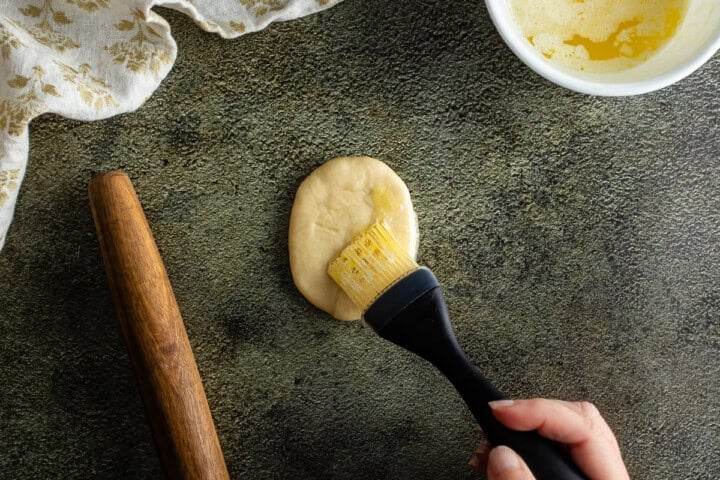 Brushing melted butter onto dough for Parker House Rolls on a textured surface.
