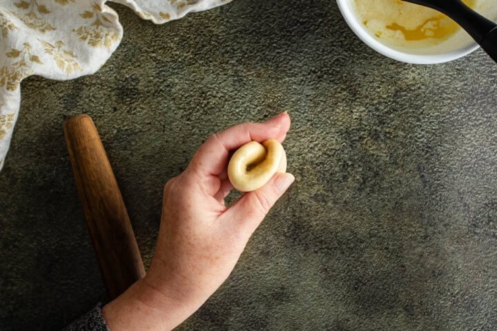 Hand shaping dough for Parker House Rolls on a textured surface with baking ingredients nearby.