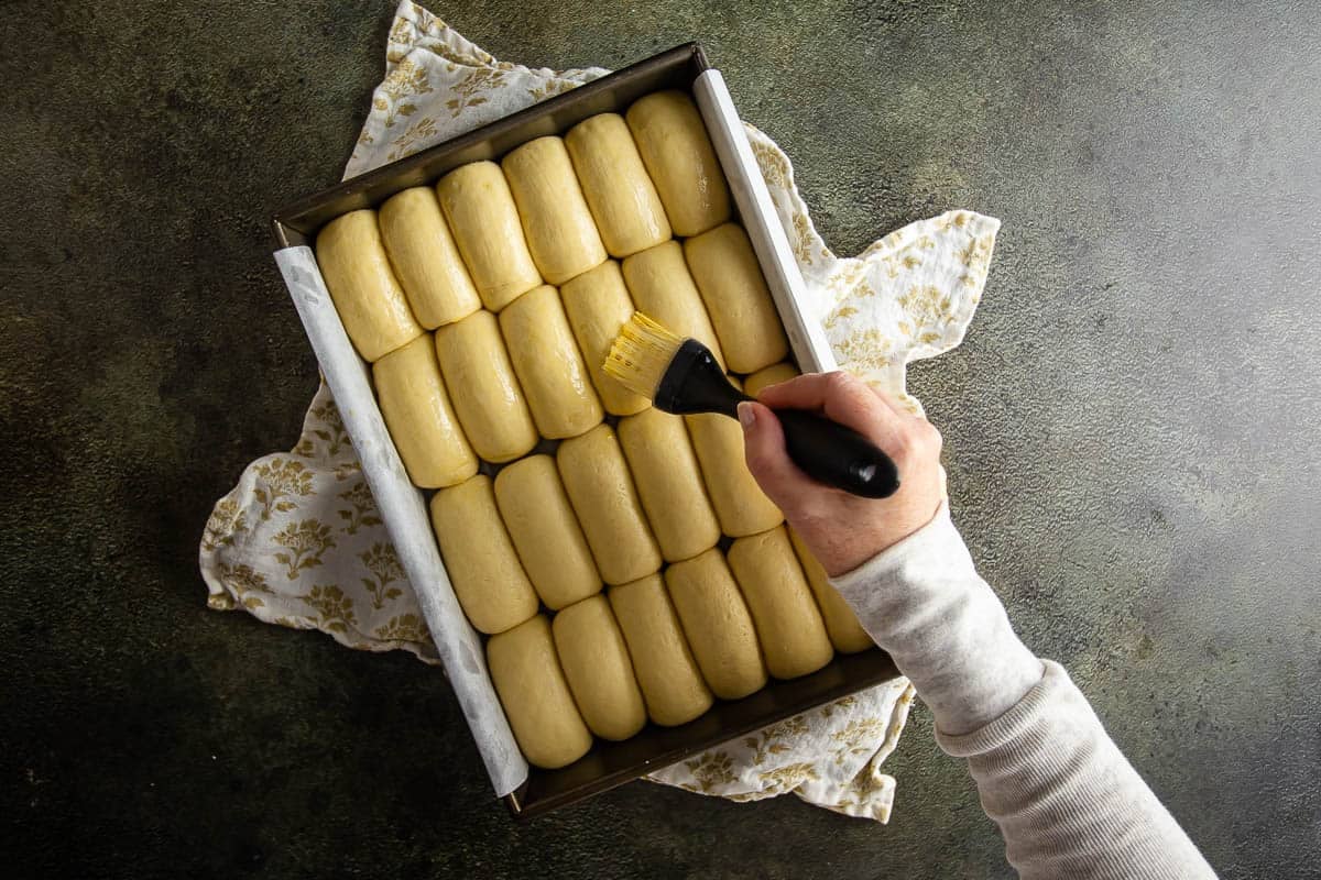 Unbaked Parker House rolls in a baking tray being brushed with egg wash.