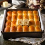Freshly baked Parker House rolls in a baking pan with one roll broken open.