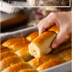 Freshly baked Parker House rolls in a baking dish with a hand picking one up.