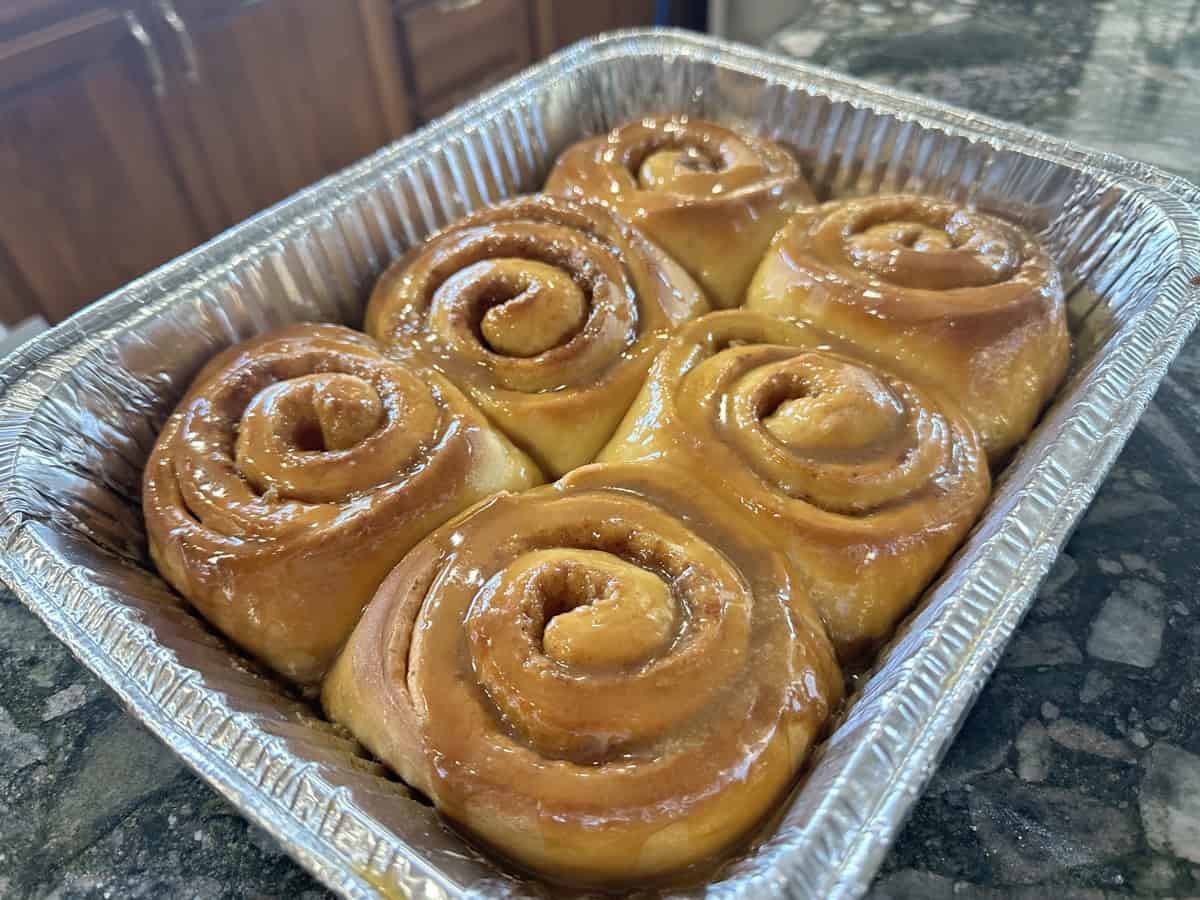 Fresh cinnamon rolls with caramel glaze in a baking tray on a kitchen counter.