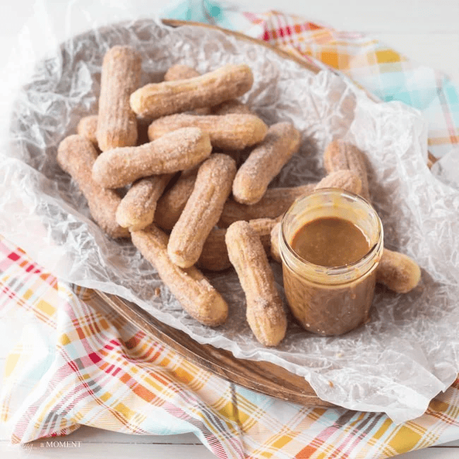 Churros with caramel dipping sauce on a rustic tray with colorful cloth background.