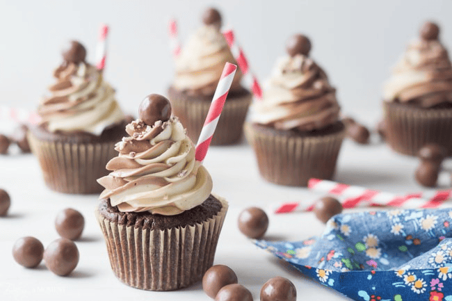 Brownie cupcakes with swirled chocolate and vanilla frosting, candy sprinkles, and striped straws.