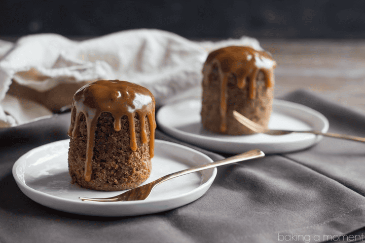Two caramel drizzled mini cakes on white plates with gold forks, dark background.