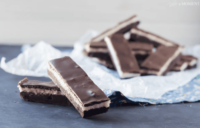 Chocolate bar desserts stacked with creamy filling on dark surface.