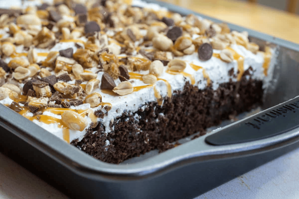 Chocolate cake with caramel, nuts, and chocolate chips on top in a baking dish.