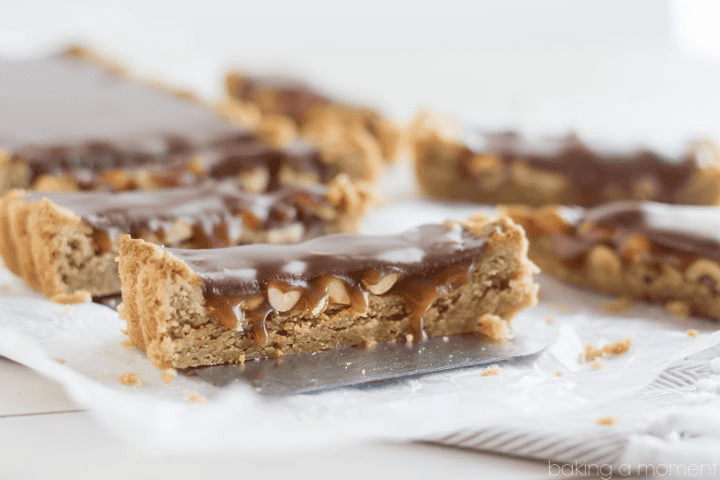 Peanut butter caramel bars with chocolate topping on parchment paper.